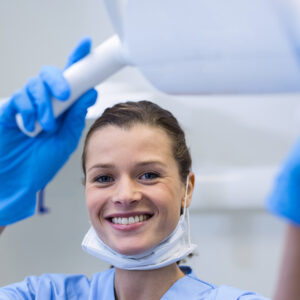 Smiling female dental professional in scrubs and gloves adjusting a bright overhead light.
