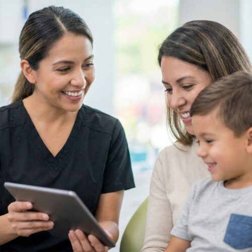 A friendly dental professional sharing information on a digital tablet with a mother and young child.