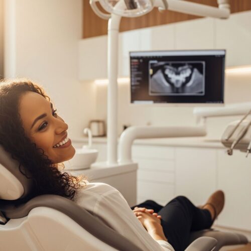 A relaxed patient smiling while reclining in a dental chair with a high-tech monitor in the background.